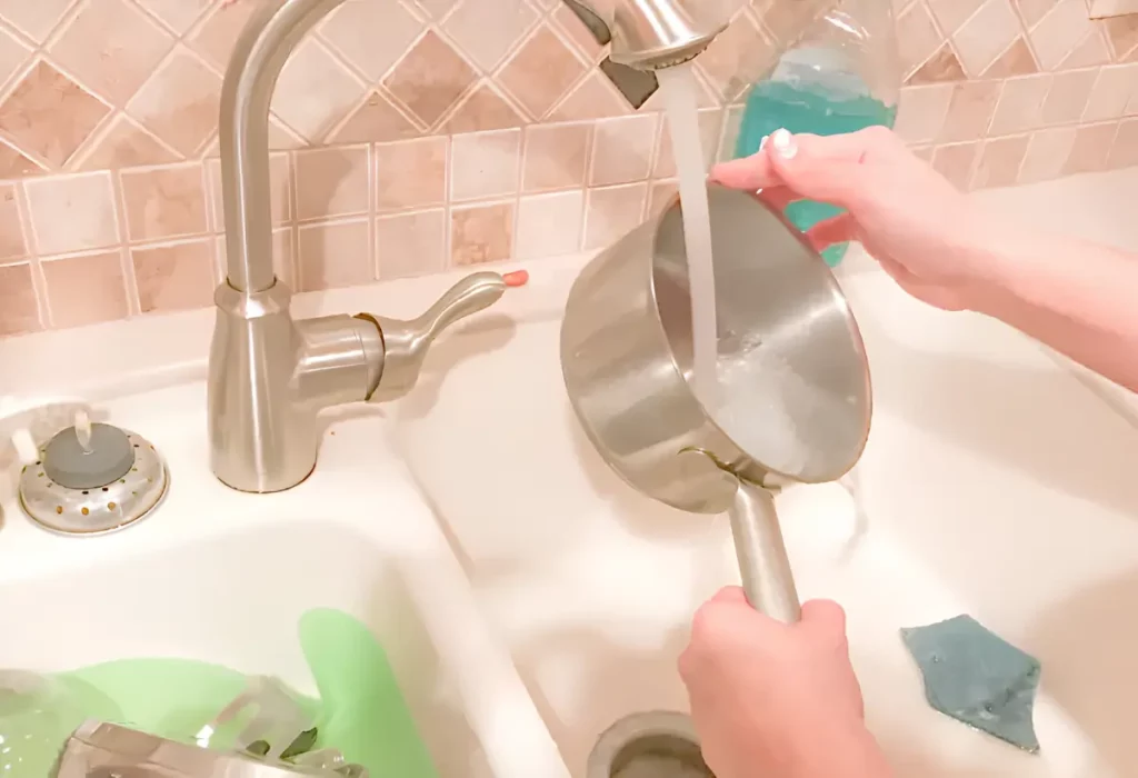 uma pessoa lavando uma panela de alumínio.