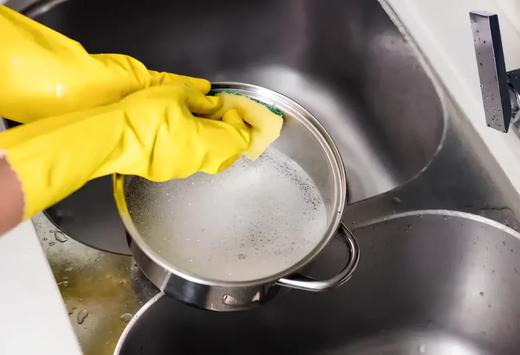 uma pessoa lavando uma panela de alumínio.