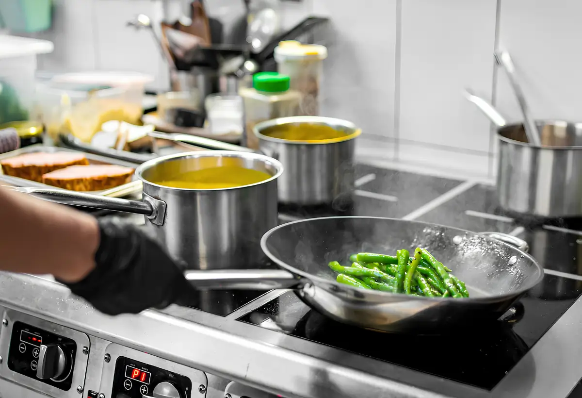 Uma pessoa cozinhando em um fogão industrial com panelas de alumínio.