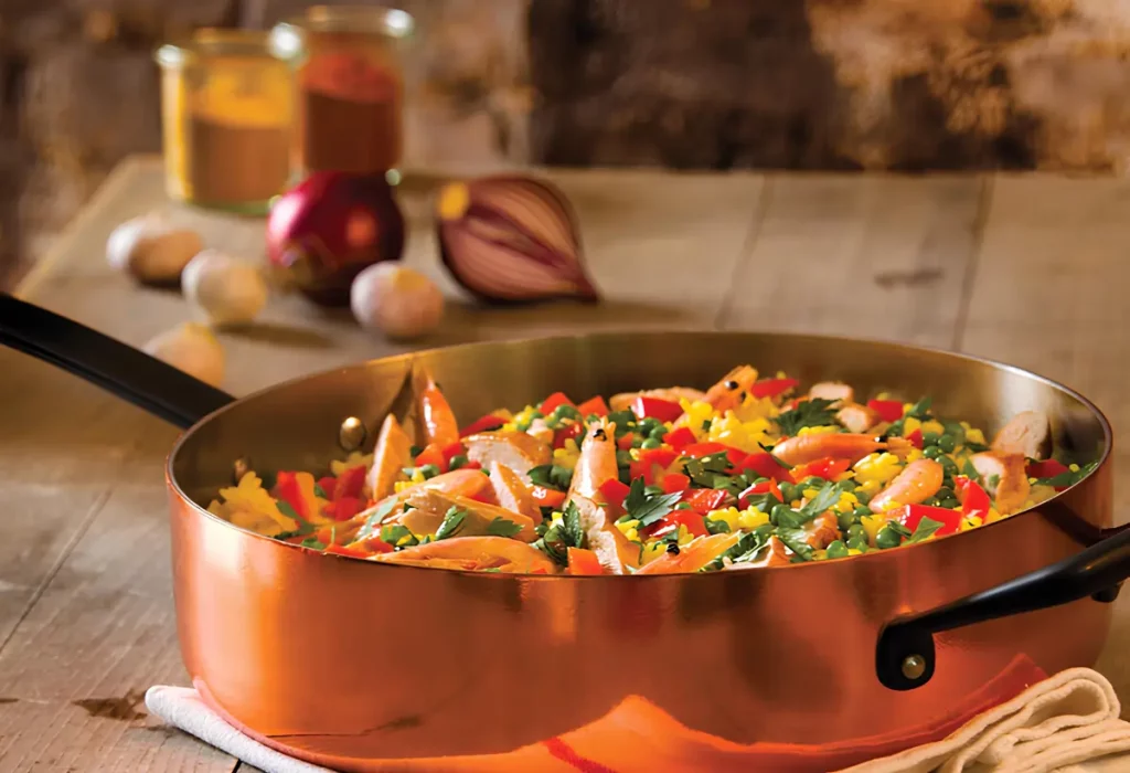 Uma panela de cobre com comida dentro em cima de uma mesa pronto para ser servido.