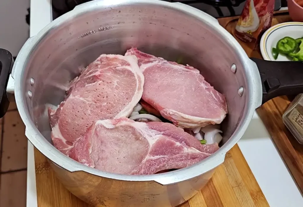 Panela de pressão com carne de bisteca dentro.