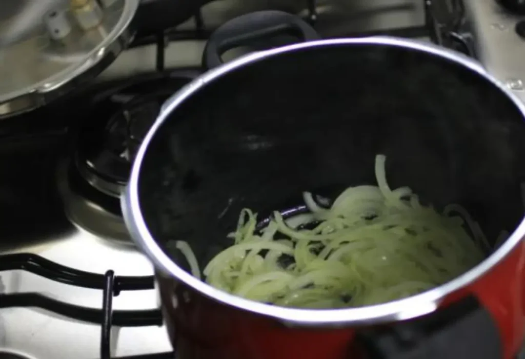 Uma panela de pressão com bife acebolado sendo feito.