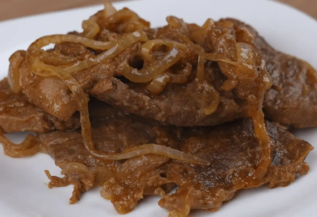 Vários pedaços de bife acebolado.