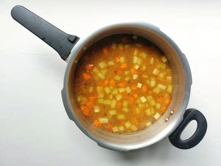 Uma panela de pressão com sopa de legumes sendo preparada.