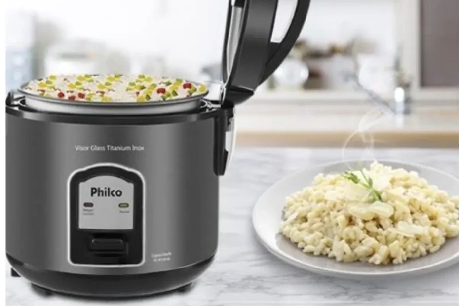 Uma panela elétrica da marca philco em uma mesa, ao lado um prato com arroz fresco.