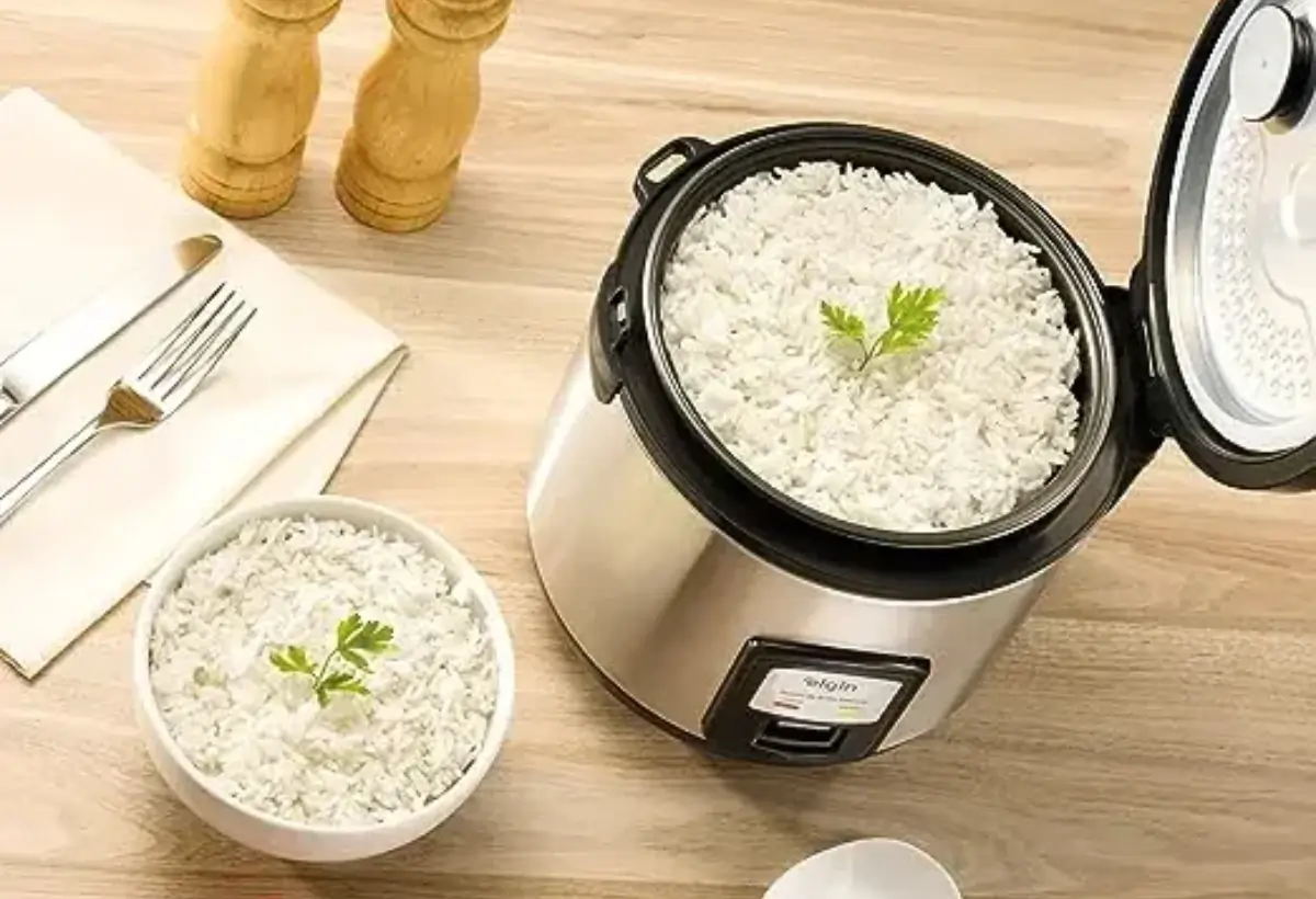 Uma panela elétrica de arroz e tigelas com arroz prontos em uma mesa.