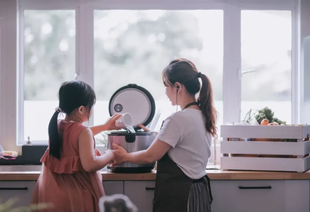 Mãe e filha fazendo arroz em uma panela elétrica.