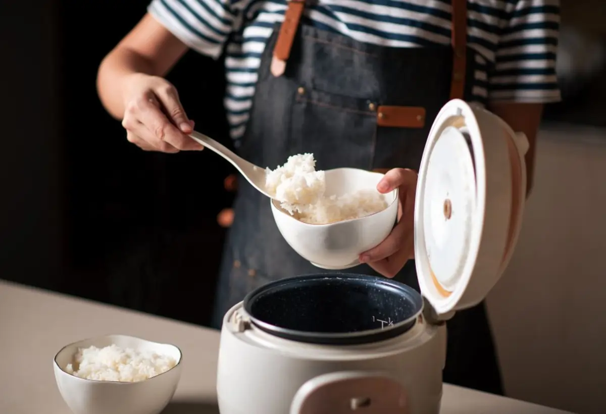 Uma pessoa fazendo arroz branco em uma panela elétrica.