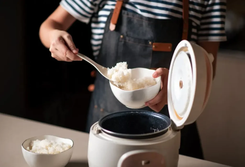 Uma pessoa fazendo arroz branco em uma panela elétrica.
